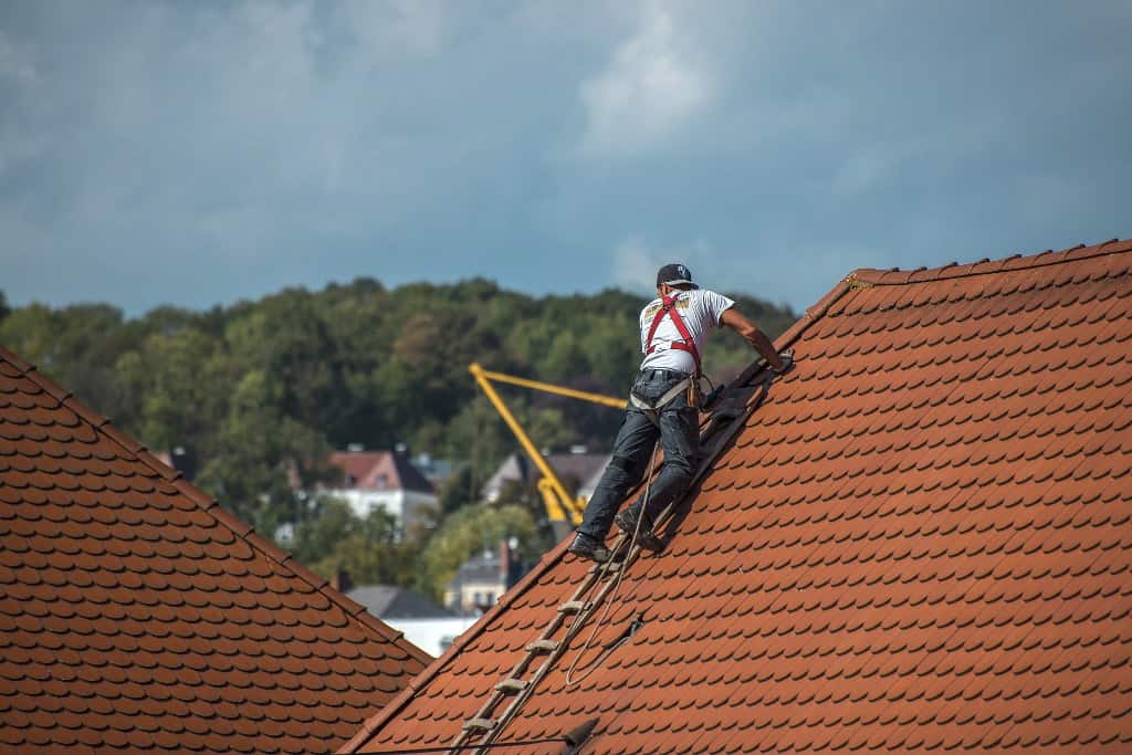 Ausbildung München Dachdecker an Steildach mit Gurt vor Häuser zwischen Bäumen und Himmel