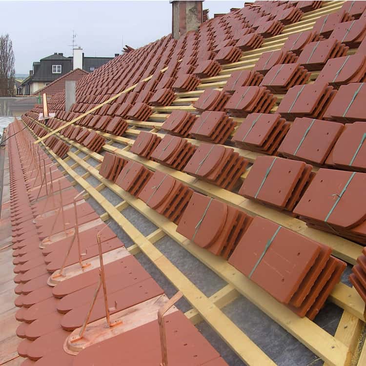 Dachdeckerei München hellrote Biberschwanzziegel in Bündel auf Dachlattung gestapelt