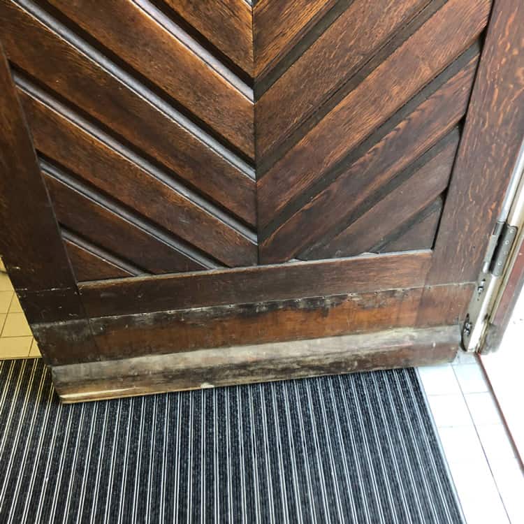 Spengler München alte Haustüre aus dunklem Holz mit abgenutztem abgesplittertem Fußbereich
