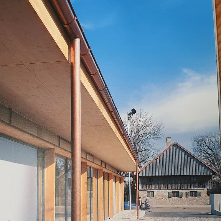 Dachdeckerei München Gebäude mit Dachrinne Ablaufrohr Kupfer an überdachtem Umlauf mit Holzfassade