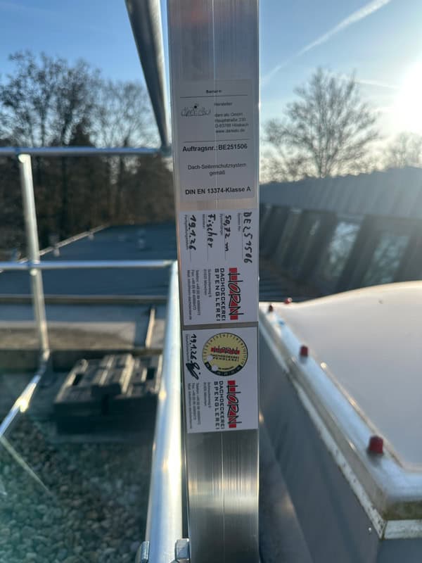 Nahaufnahme einer Wartungsplakette von Firma Horn auf montiertem Seitensturzgeländer zur Dachsicherheit in München