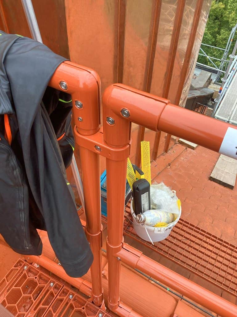 Nahaufnahme von Laufsteg mit Geländer und Tritten am Dachzugang, daneben Kamin mit Kupferverkleidung in München